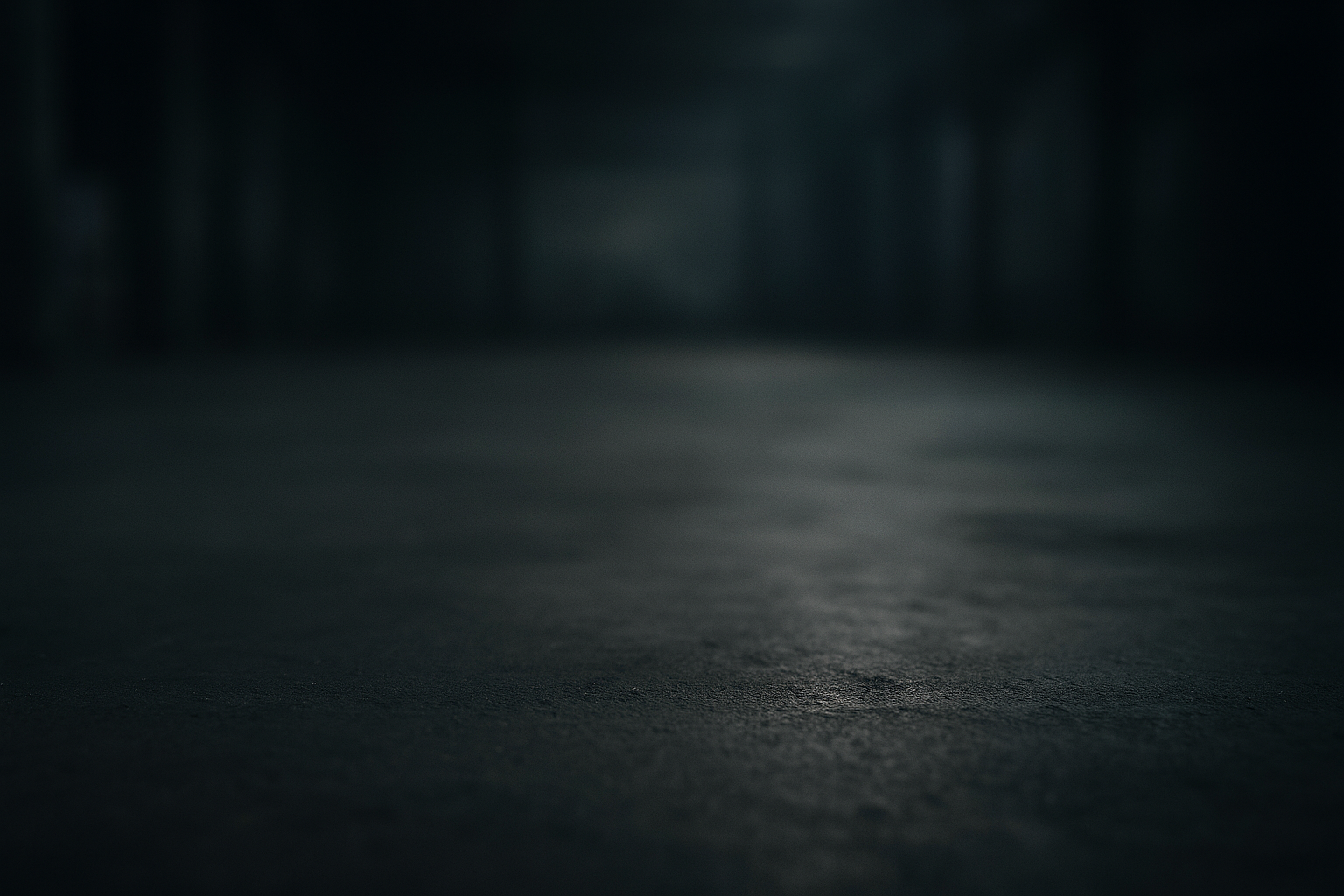 Dimly lit, empty industrial space with a textured concrete floor fading into darkness.