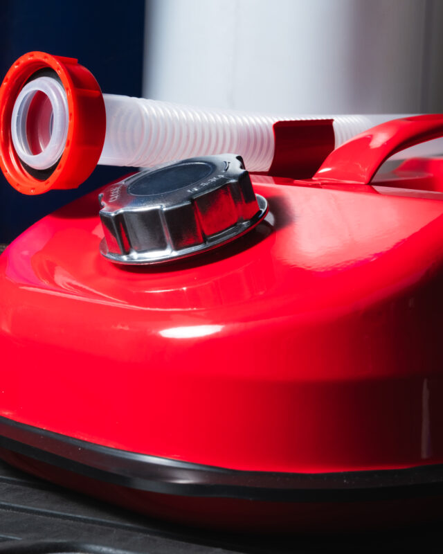 Close-up of a red fire extinguisher with a white corrugated hose and black valve cap.