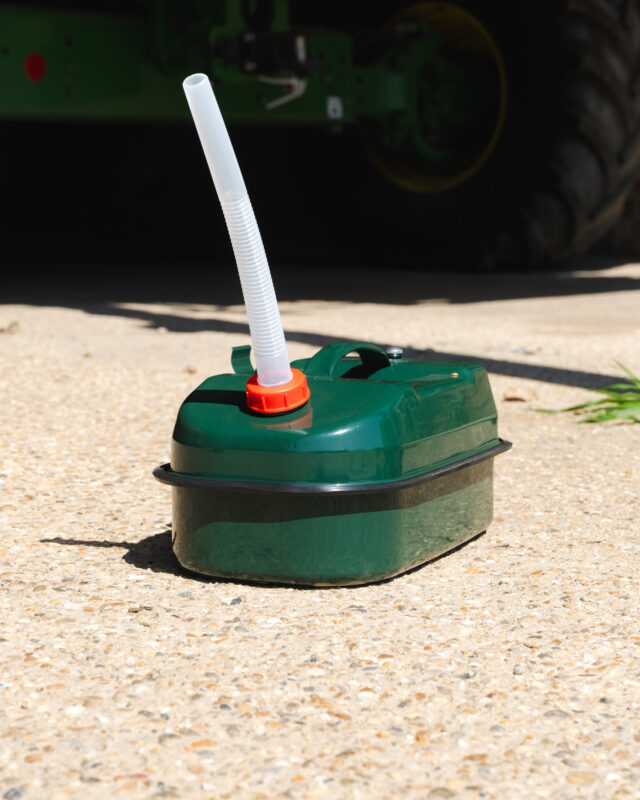 Close-up of a green liquid container with a white corrugated nozzle attached to an orange cap on a concrete surface.