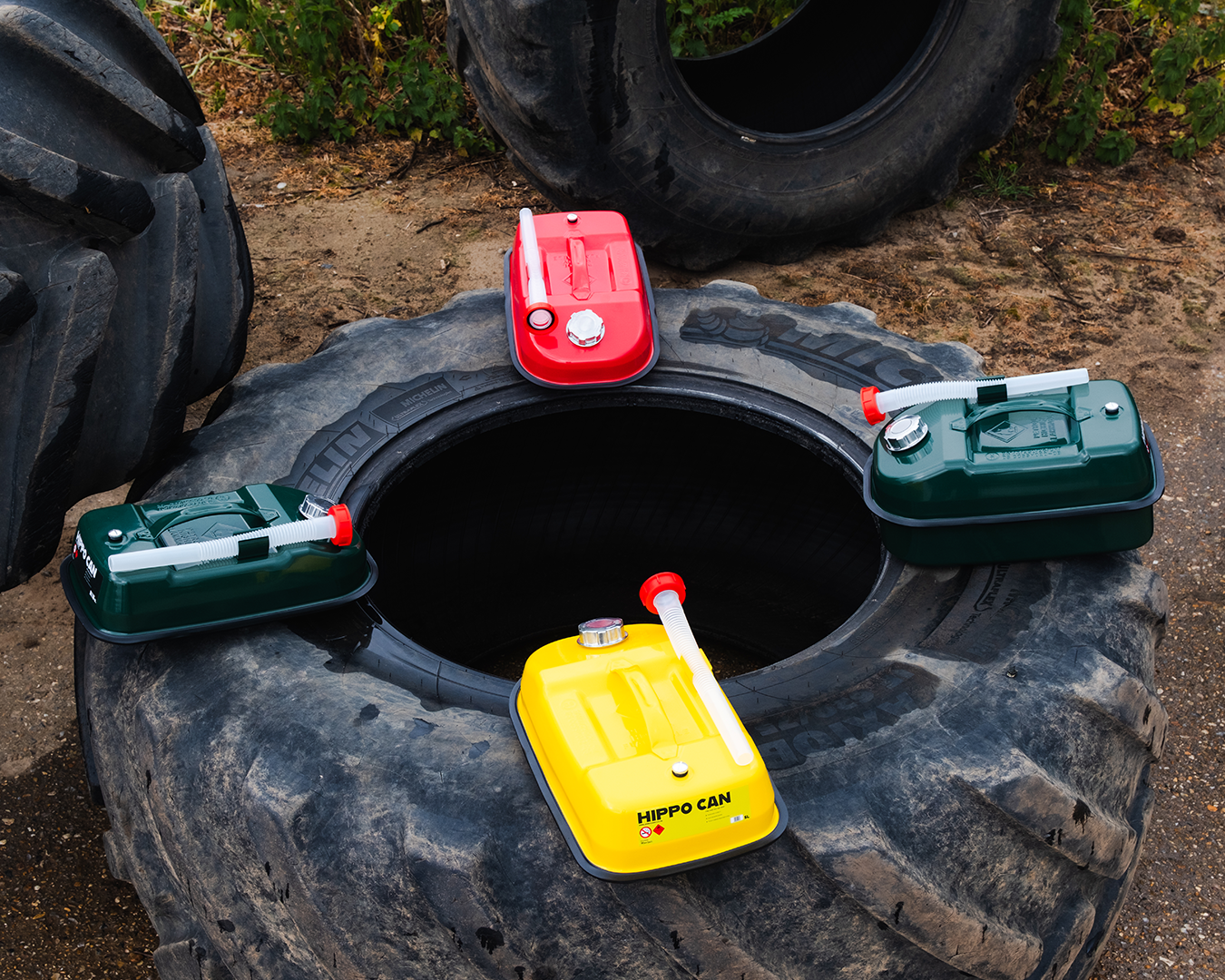 Colorful plastic fuel cans arranged around an open tire on muddy ground, outdoors.